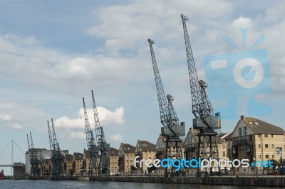 Old Dockside Cranes Alongside A Waterfront Development Stock Photo