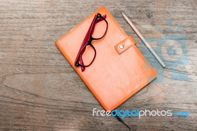 Orange Diary With Pencil And Eye Glasses On Wood Table Stock Photo