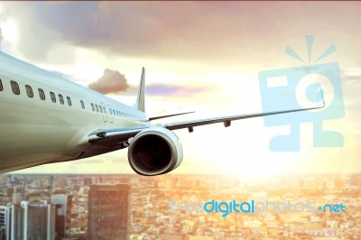 Passenger Plane Flying Over City Building And Sun Light On Background Stock Photo