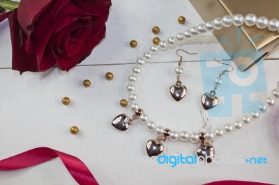 Pearl Necklace With Golden Gift, Red Rose And Rd Ribbon On White Wood Stock Photo