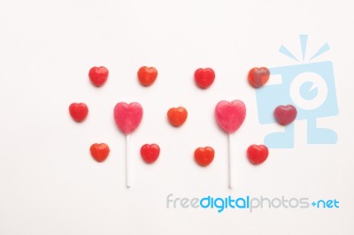 Pink Valentine's Day Heart Shape Lollipop With Small Red Candy In Cute Pattern On Empty White Paper Background. Love Concept. Colorful Hipster Style. Knolling Top View Stock Photo
