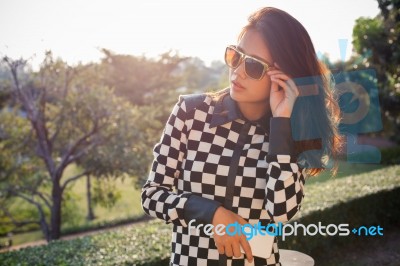 Portrait Of Beautiful Chick Fashion Woman Wearing Sun Glasses And Smartphone In Hand Against Afternoon Light With Blur Background And Copy Space Stock Photo