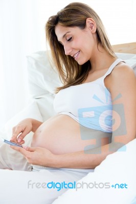 Pregnant Woman Using Her Mobile Phone On Sofa Stock Photo