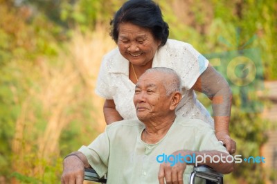 Senior Woman Pushing Her Disabled Husband On Wheelchair Stock Photo