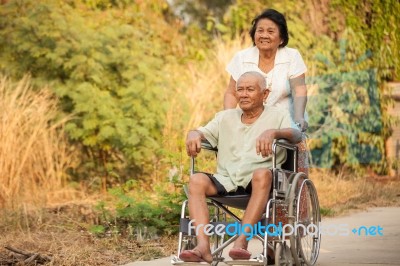 Senior Woman Pushing Her Disabled Husband On Wheelchair Stock Photo