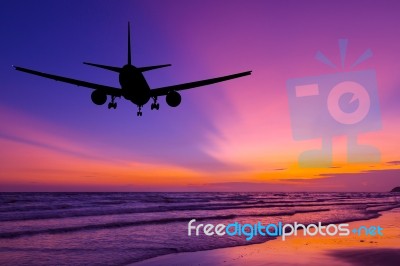 Silhouetted Commercial Airplane Flying Above The Sea At Sunset Stock Photo