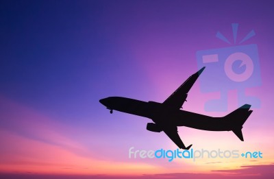 Silhouetted Commercial Airplane Flying At Sunset Stock Photo