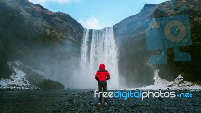 Skogafoss Waterfall In Iceland. Guy In Red Jacket Looks At Skogafoss Waterfall Stock Photo