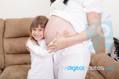 Smiling Girl Listening To The Abdomen Of Her Mother Stock Photo