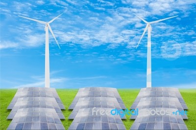 Solar Panels And Wind Turbine On Green Grass Field Against Blue Stock Photo