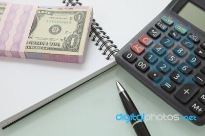 Stack Of Bank Note And Pen Calculater On Note Book Stock Photo