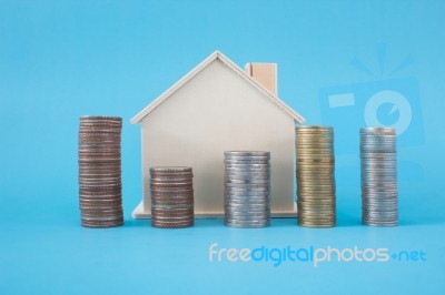 Stack Of Coins And Wooden House Symbol On Blue Soft Background Stock Photo