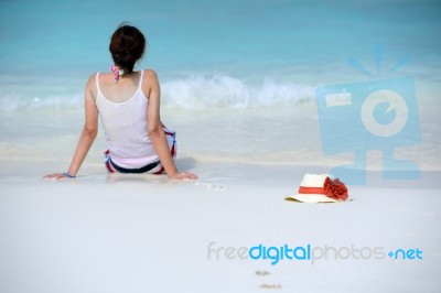 The Hat Is Beside Woman Sitting On The Beach Stock Photo