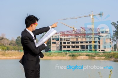 The Young Businessman Holds A Blueprint And Points To The Struct… Stock Photo