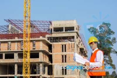 The Young Engineer Holds The Blueprint Over Building Being Built… Stock Photo