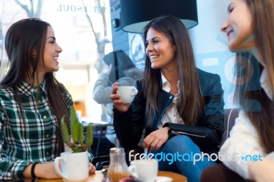 Three Young Woman Drinking Coffee And Speaking At Cafe Shop Stock Photo