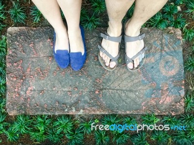 Top View Feet Of Male And Female Couple Lover Standing On Stone Floor Among Little Green Grass Garden. Hipster Style Stock Photo