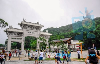 Tourists At The Gate To Po Lin Monastery With Tian Tan Buddha Statue Up On The Hill In Background, Ngong Ping Village, Lantau Island, Hong Kong Stock Photo