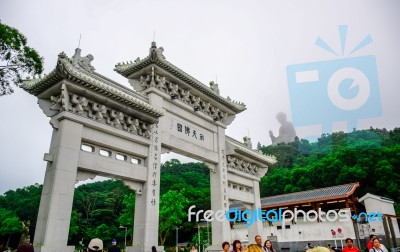 Tourists At The Gate To Po Lin Monastery With Tian Tan Buddha Statue Up On The Hill In Background, Ngong Ping Village, Lantau Island, Hong Kong Stock Photo