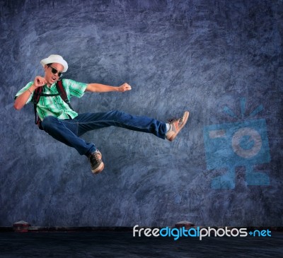 Traveling Man Jumping Mid Air With Exciting Emotion Against Cement Wall Stock Photo