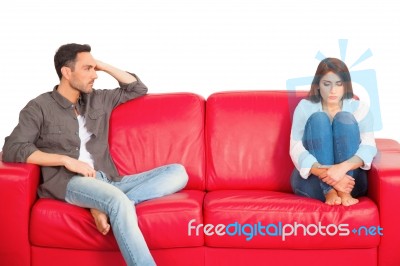 Unhappy Young Couple Sitting On Red Sofa Stock Photo