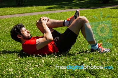 Urban Athlete Doing Stretching Exercises On The Grass Stock Photo