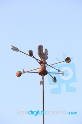 Weather Vane Compass Over House Roof Against Blue Sky Background… Stock Photo