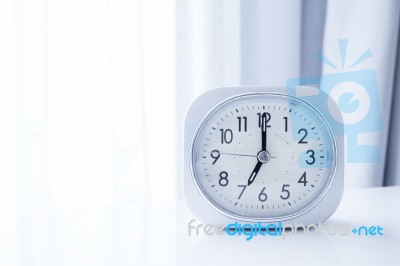 White Square Clock On White Bed Stand With White Curtain Background, Morning Time In Minimal Style Decoration Stock Photo