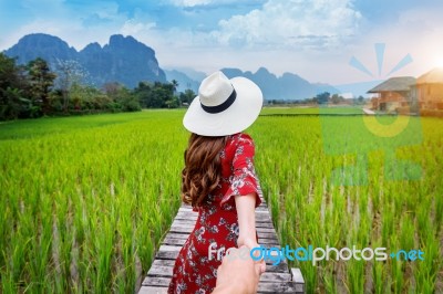 Woman Holding Man's Hand And Leading Him To Wooden Path And Green Rice Field In Vang Vieng, Laos Stock Photo
