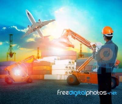 Working Man In Logistic Business Working In Container Shipping Yard With Dusky Sky And Jet Plane Cargo Flying Above Use For Land To Air Transport And Freight Stock Photo