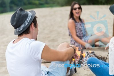Young Adult Friends Hanging Around At Bonfire On Sandy Beach Stock Photo