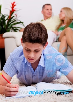 Young Boy Studying With Family In The Background Stock Photo