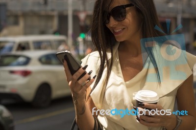 Young Brunette Laughs Into Phone, Hod Coffee In Another Hand Stock Photo