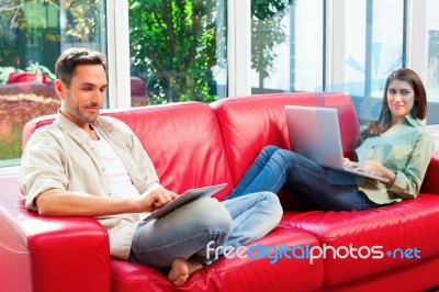 Young Couple Using Digital Tablet And Laptop On Sofa Stock Photo