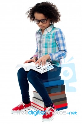 Young Kid Sitting On Stack Of Books And Reading Stock Photo