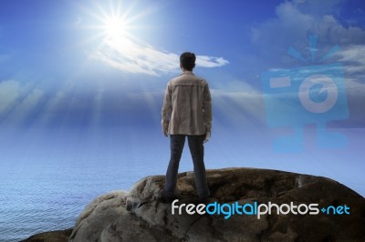 Young Man Standing On Rock Mountain And Looking To The Sun Stock Photo
