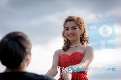 Young Woman In Red Dress Is Holding Hands With Young Man Stock Photo