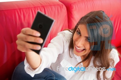 Young Woman Making Face While Taking Selfie On Sofa Stock Photo