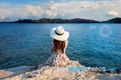 Young Woman Sitting On The Top Of Rock And Looking At The Seashore Stock Photo