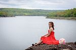 Beautiful Red Dress Girl Sitting On The River And Mountains Stock Photo