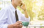 Business Man Using Mobile Phone And Hold A Cup While Sitting In Stock Photo
