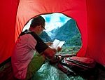 Camping Man Reading Traveling Guide Book In Camp Tent Against Beautiful Scenic Of Glacier Mountain Stock Photo