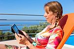 Caucasian Woman On Sunlounger Reading Tablet Stock Photo