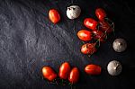 Cherry Tomatoes With Garlic On The Black Stone Table Stock Photo