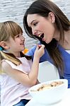 Child Eating Cereals With Her Mom In The Kitchen Stock Photo