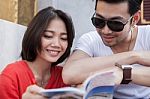 Couples Of Asian Younger Traveling Man And Woman Reading A Guide Book With Happiness Face Toothy Smile Stock Photo
