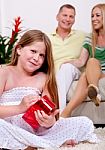 Cute Girl Opening Christmas Gift With Parents In The Background Stock Photo