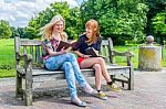 Dutch Girls Sitting On Wooden Bench In Park Reading Books Stock Photo