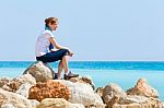 Dutch Woman Sitting On Rocks With Blue Sea Horizon Stock Photo