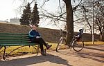Elderly Man Sitting On A Bench Near His Bicycle In A City Park Stock Photo